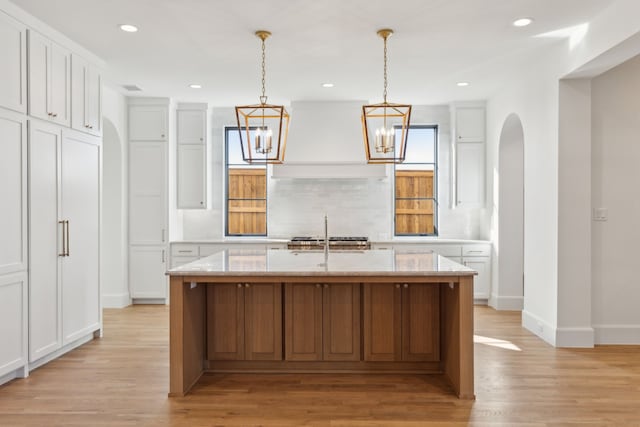 kitchen with white cabinets, custom range hood, a kitchen island with sink, and tasteful backsplash