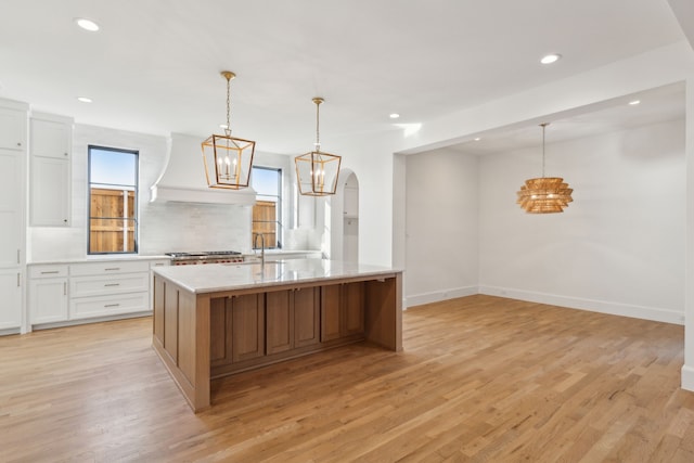 kitchen featuring white cabinets, a kitchen island with sink, light hardwood / wood-style flooring, and hanging light fixtures