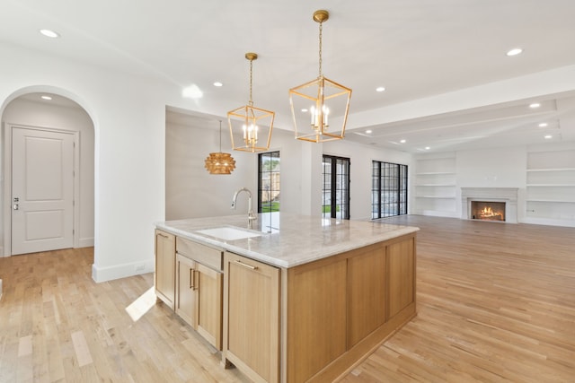 kitchen featuring pendant lighting, an island with sink, sink, built in features, and light stone counters