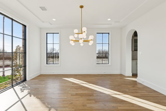 unfurnished dining area with plenty of natural light, hardwood / wood-style floors, and a notable chandelier