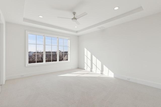 unfurnished room featuring ceiling fan, light carpet, and a raised ceiling