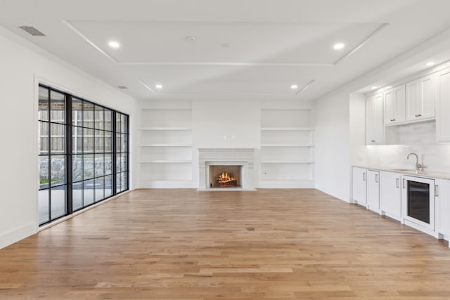 unfurnished living room featuring sink, built in features, light hardwood / wood-style flooring, and wine cooler