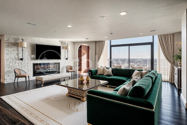 living area featuring a wall of windows, wood finished floors, visible vents, arched walkways, and a glass covered fireplace