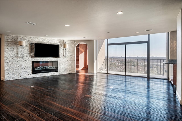 unfurnished living room with wood finished floors, visible vents, arched walkways, and expansive windows