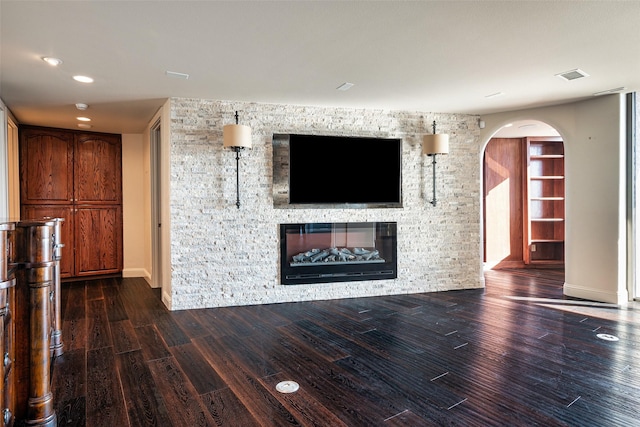 unfurnished living room with a stone fireplace, visible vents, wood finished floors, and arched walkways