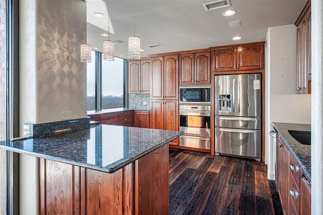 kitchen with dark stone countertops, pendant lighting, dark wood-type flooring, backsplash, and stainless steel appliances