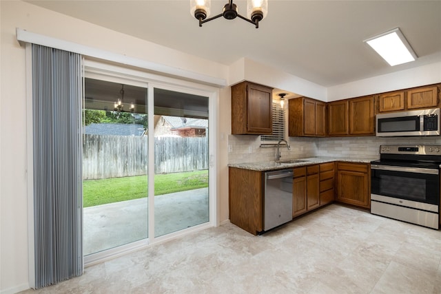 kitchen featuring sink, light stone countertops, an inviting chandelier, decorative backsplash, and stainless steel appliances