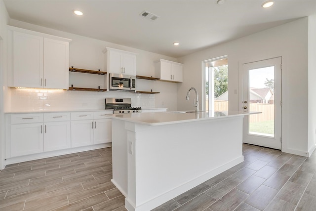 kitchen with white cabinets, a kitchen island with sink, appliances with stainless steel finishes, and plenty of natural light