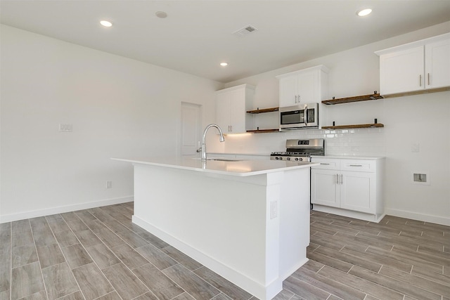 kitchen with sink, stainless steel appliances, white cabinets, and an island with sink