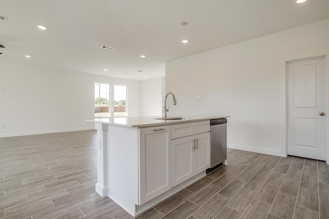 kitchen featuring sink, dishwasher, white cabinetry, and a center island with sink