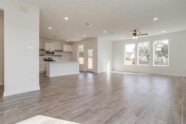 unfurnished living room with sink, ceiling fan, and plenty of natural light