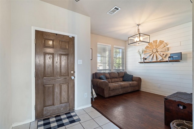 tiled foyer entrance featuring wood walls and a notable chandelier