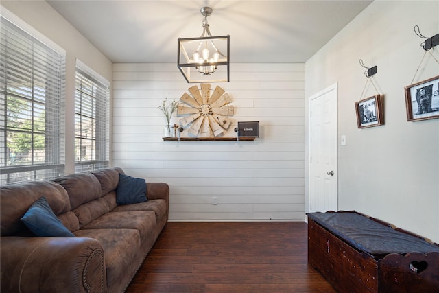 living room with dark hardwood / wood-style floors, wood walls, and an inviting chandelier