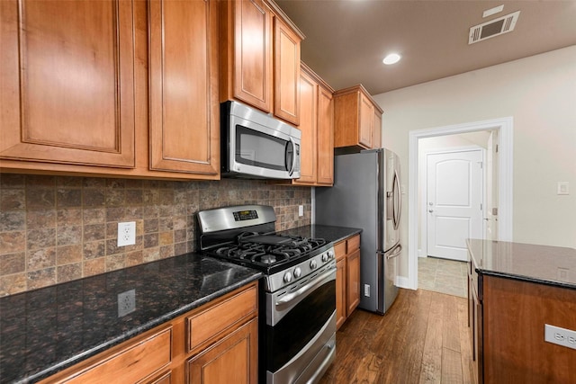 kitchen with dark stone countertops, appliances with stainless steel finishes, dark hardwood / wood-style flooring, and tasteful backsplash