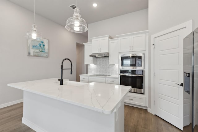 kitchen with light stone countertops, built in microwave, stainless steel oven, and an island with sink