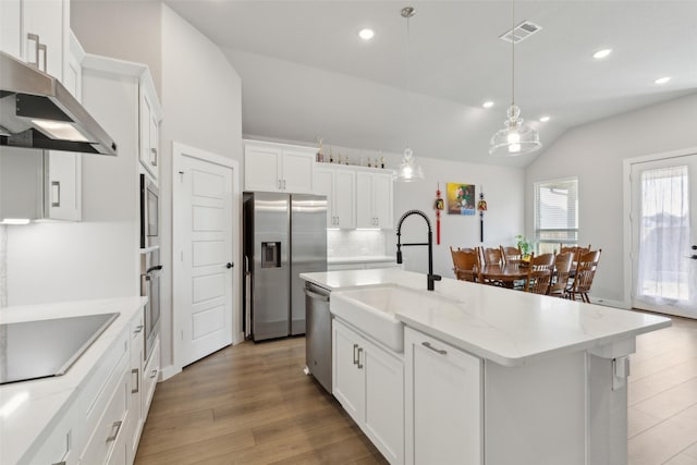 kitchen featuring pendant lighting, white cabinetry, stainless steel appliances, a kitchen island with sink, and vaulted ceiling