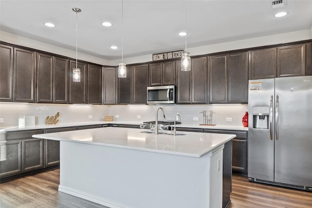 kitchen featuring a kitchen island with sink, hanging light fixtures, dark hardwood / wood-style flooring, and appliances with stainless steel finishes