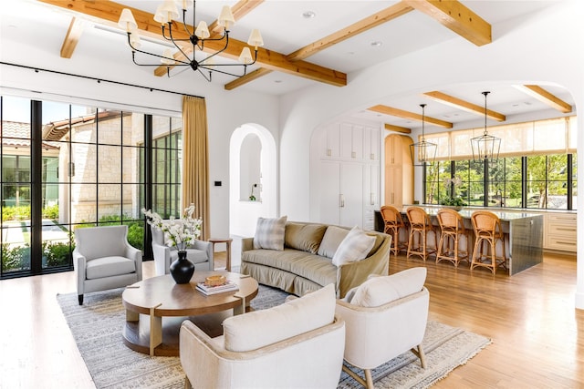 living room with an inviting chandelier, plenty of natural light, light hardwood / wood-style flooring, and beamed ceiling