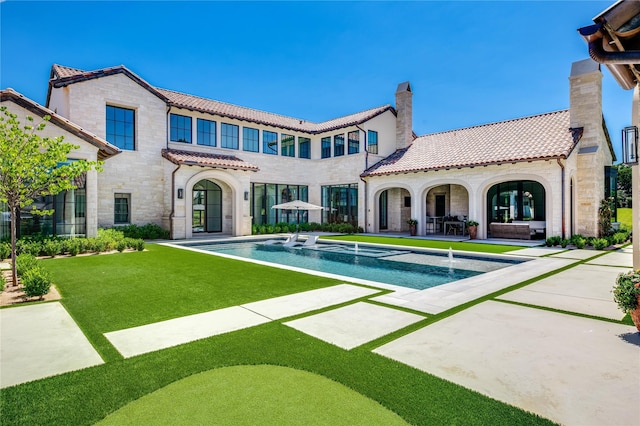 rear view of house featuring pool water feature, a patio, and a lawn