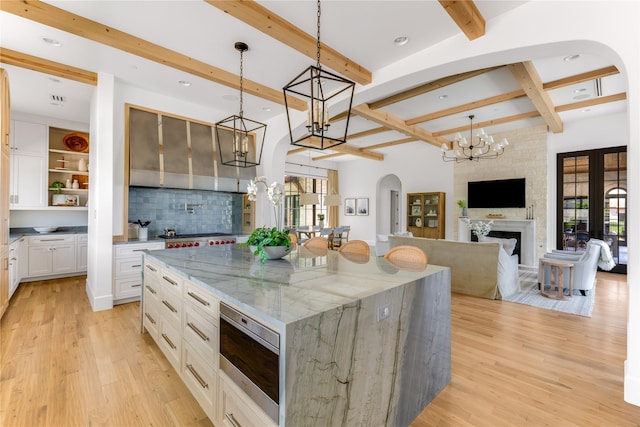 kitchen featuring a large island, white cabinetry, hanging light fixtures, light stone counters, and stainless steel microwave