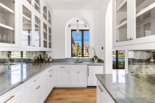 bar with dark stone counters, a wealth of natural light, light wood-type flooring, and white cabinets