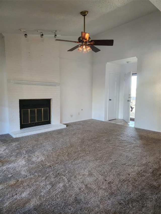 unfurnished living room with rail lighting, a textured ceiling, ceiling fan, a brick fireplace, and light colored carpet