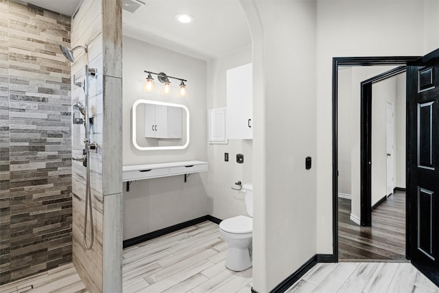 bathroom featuring toilet, tiled shower, and wood-type flooring