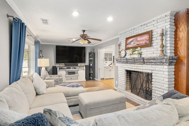 living area with visible vents, light wood-style flooring, ornamental molding, a fireplace, and recessed lighting