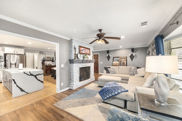 living room with a textured ceiling, ornamental molding, ceiling fan, a fireplace, and light hardwood / wood-style floors