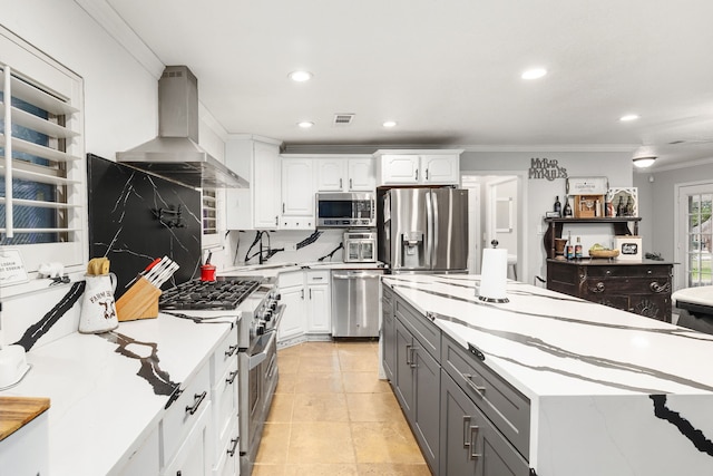 kitchen featuring gray cabinets, white cabinetry, stainless steel appliances, ornamental molding, and wall chimney exhaust hood