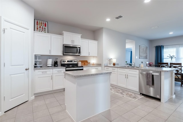 kitchen featuring appliances with stainless steel finishes, white cabinetry, light tile patterned floors, sink, and a kitchen island