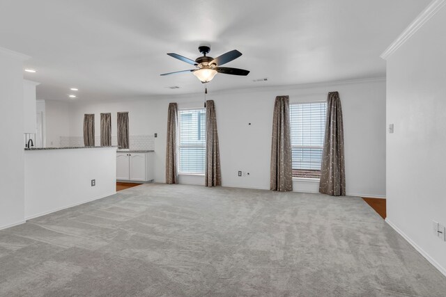 unfurnished living room with ceiling fan, ornamental molding, and light carpet