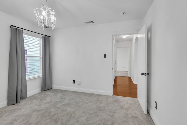 unfurnished room with light carpet and an inviting chandelier