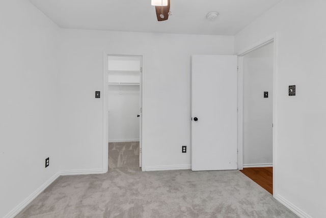 unfurnished bedroom with a spacious closet, light colored carpet, a closet, and ceiling fan