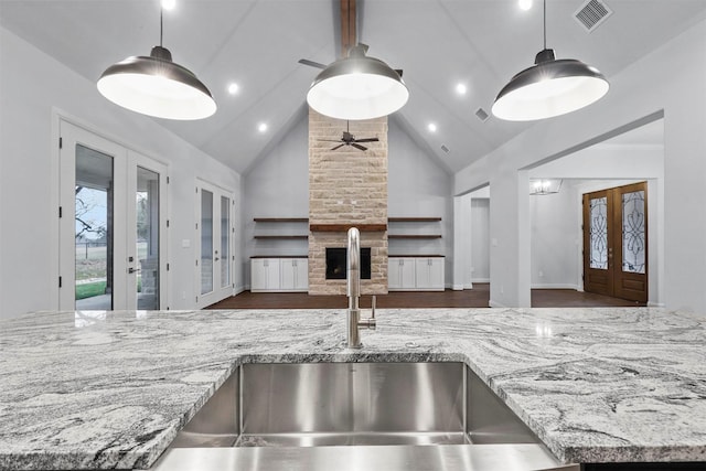 kitchen featuring hanging light fixtures, french doors, light stone counters, a fireplace, and high vaulted ceiling