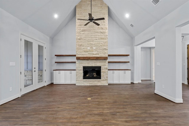 unfurnished living room featuring a stone fireplace, french doors, high vaulted ceiling, dark hardwood / wood-style flooring, and ceiling fan