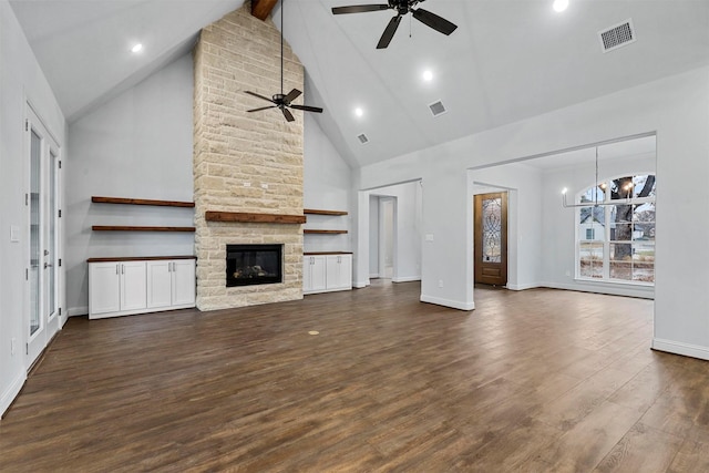 unfurnished living room featuring a stone fireplace, high vaulted ceiling, beam ceiling, dark wood-type flooring, and ceiling fan with notable chandelier