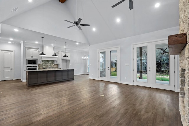 unfurnished living room with ceiling fan with notable chandelier, beam ceiling, high vaulted ceiling, and dark hardwood / wood-style flooring