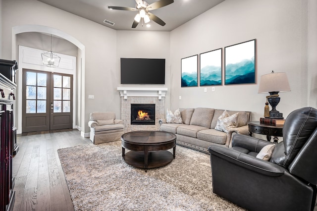 living room with a fireplace, hardwood / wood-style floors, ceiling fan with notable chandelier, and french doors