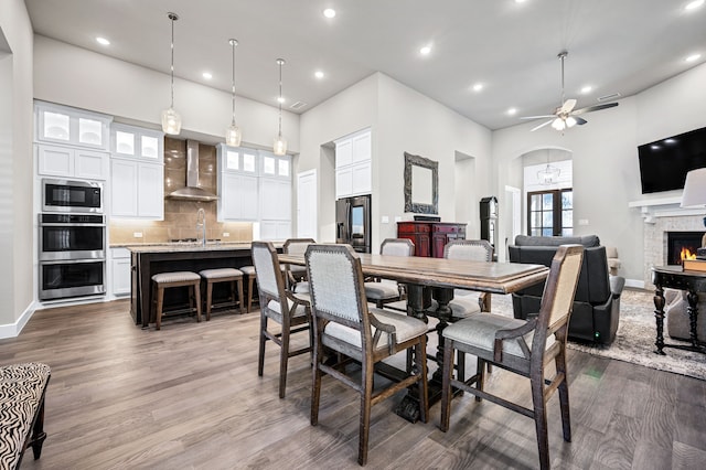 dining room featuring ceiling fan, sink, dark wood-type flooring, a towering ceiling, and a stone fireplace