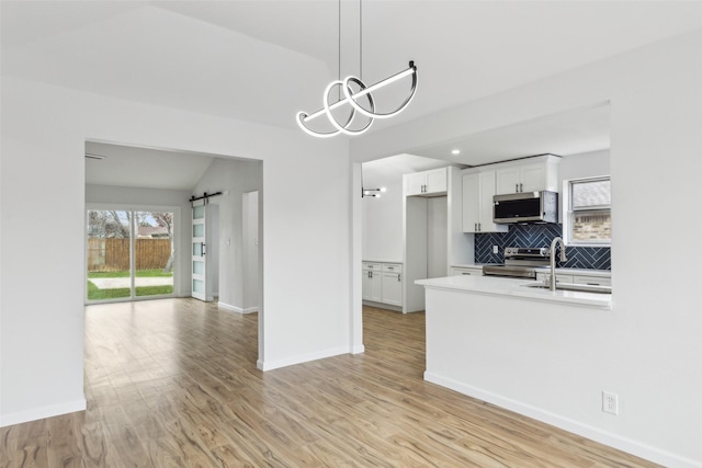 kitchen featuring a barn door, white cabinets, decorative light fixtures, backsplash, and stainless steel appliances