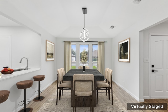 dining area with sink, vaulted ceiling, and light wood-type flooring