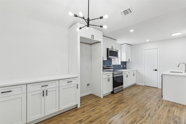 kitchen featuring stainless steel appliances, white cabinetry, light hardwood / wood-style floors, and decorative backsplash