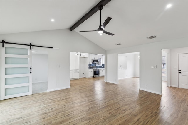 unfurnished living room with ceiling fan, beam ceiling, a barn door, and light wood-type flooring