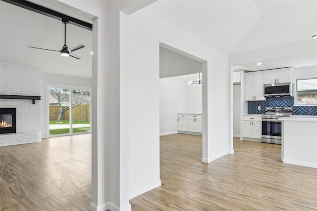 interior space with a brick fireplace, light hardwood / wood-style floors, lofted ceiling, and ceiling fan