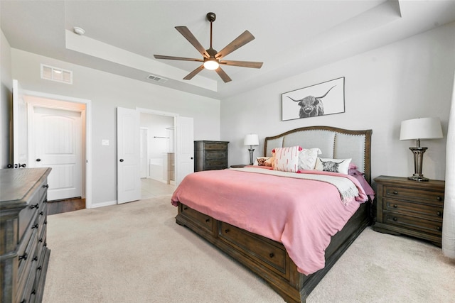 bedroom featuring ceiling fan, connected bathroom, light colored carpet, and a tray ceiling