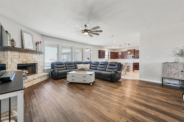 living room featuring ceiling fan, a fireplace, dark wood-type flooring, and a textured ceiling