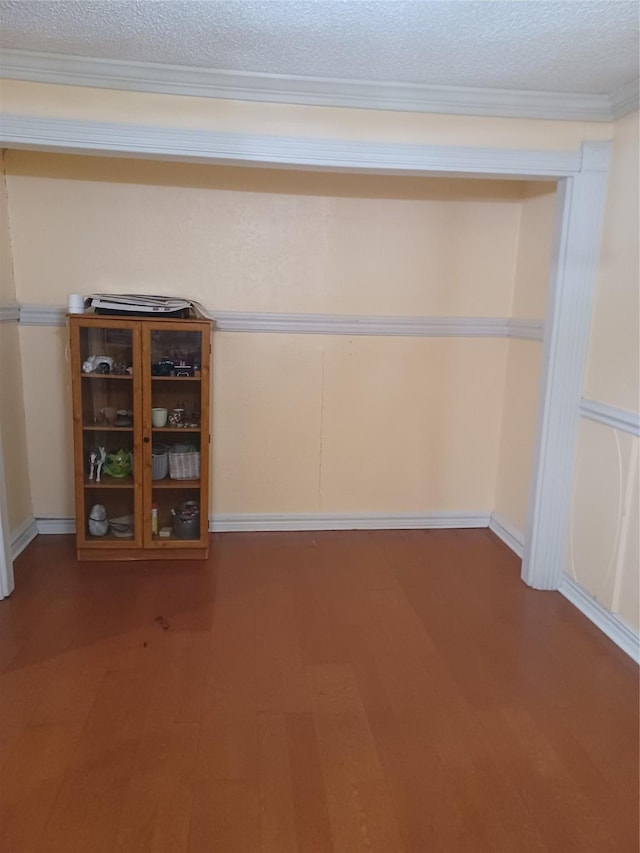 interior space with baseboards, a textured ceiling, ornamental molding, and wood finished floors