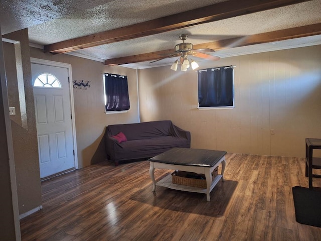 living room featuring dark wood-type flooring, beamed ceiling, a textured ceiling, and ceiling fan