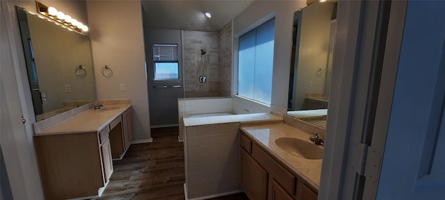 full bathroom with a tile shower, wood finished floors, two vanities, and a sink